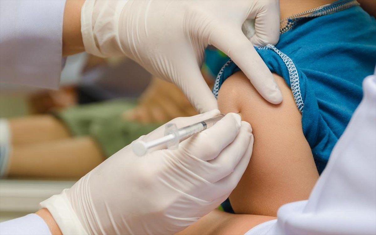 Νοσηλευτής εμβολιάζει ένα παιδί στον ώμο