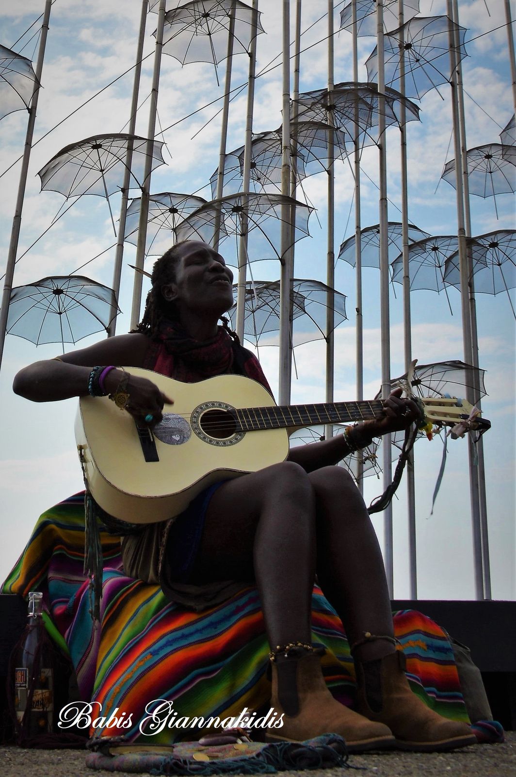 Κοπέλα παιζει κιθάρα κάτω από το γλυπτό Ομπρέλλες του Ζογγολόπουλου