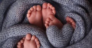 τρία ζευγάρια πατουσάκια μωρών ανάμεσα σε γκρι κουβέρτα