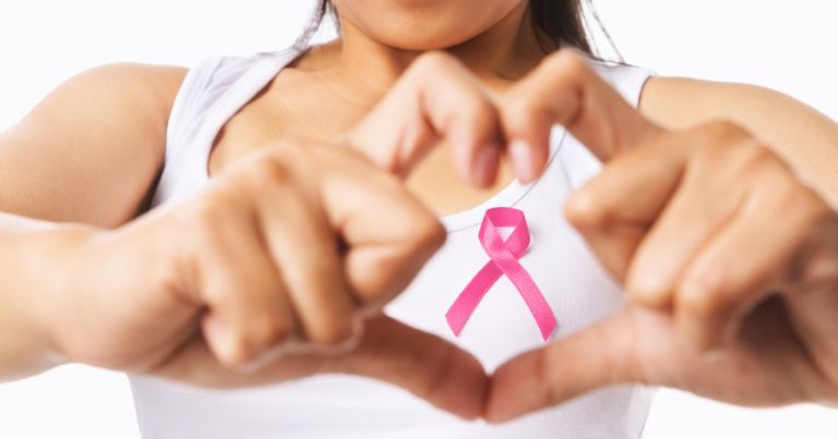 κοπέλα σχηματίζει καρδιά με τα δάχτυλά της και μέσα φαίνεται η ροζ κορδέλα του καρκίνου του μαστού