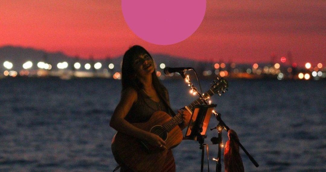 Γυναίκα πλανόδιος καλλιτέχνης παίζει κιθαρα και τραγουδα στη παραλία