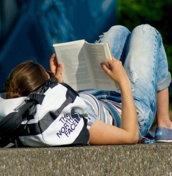 Κοπέλα που διαβάζει ξαπλωμένη σε πεζούλι