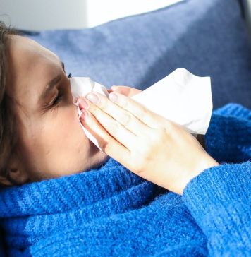 Κοπέλα με γρίπη και συνάχι σκουπίζει τη μύτη της με χαρτομάνδυλο