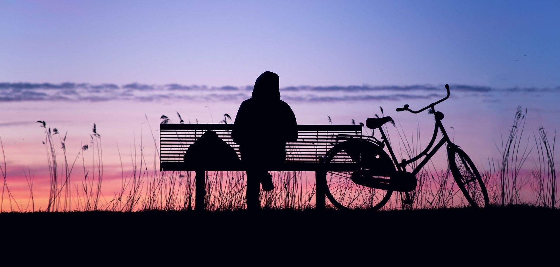 Μοναχικό άτομο καθεται σε παγκάκι ατενίζοντας το ηλιοβασίλεμα