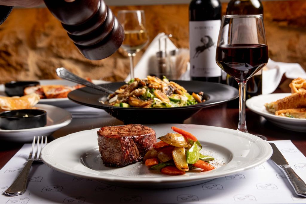 Στρωμένο τραπέζι με κύριο πιάτο Bon Fillet με λαχανικά σοτέ και υπέροχο κόκκινο κρασί