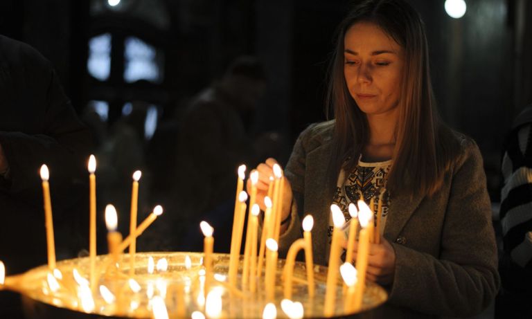 Νεαρή γυναίκα ανάβει κερί μέσα σε εκκλησία