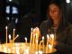 Νεαρή γυναίκα ανάβει κερί μέσα σε εκκλησία