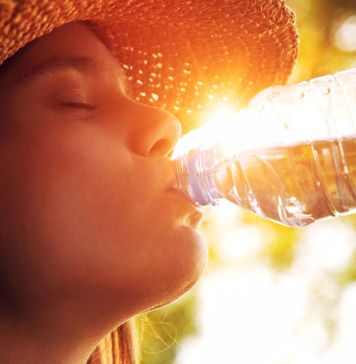 Νεαρά γυναίκα κάτω απο τον ήλιο ξεδιψά πίνοντας νερό απο μπουκάλι