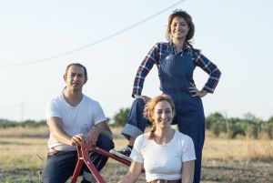 Οι τρεις ηθοποιοί ποζάρουν σε αγροτικό τοπίο πάνω σε παλιό γεωργικό εργαλείο, φωτογραφία της παράστασης Ο Ποντικός της Πόλης και ο Ποντικός της Εξοχής